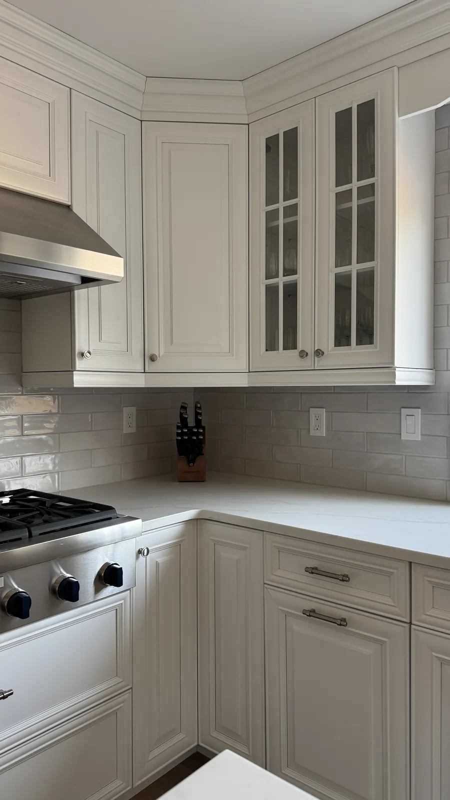 Kitchen corner with a glazed gray subway tile backsplash, a range top and white cabinets with glass-front doors