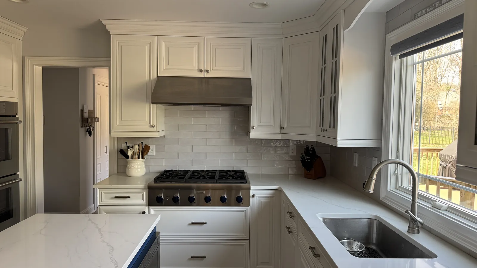 Wide view of a kitchen with a glazed gray subway tile backsplash behind the range, a window over the sink and a white quartz island