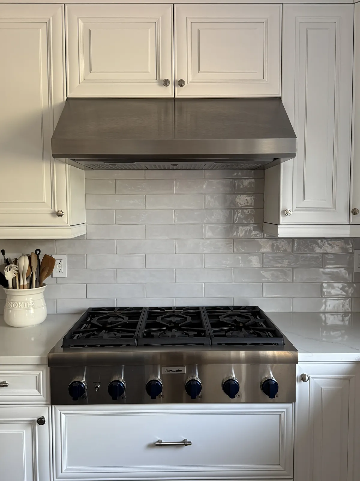 Kitchen backsplash in white glazed brick-style tile behind a stainless range and hood