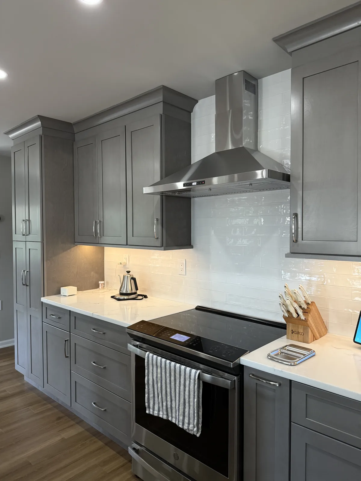Kitchen backsplash in glossy white subway tile behind a chimney hood, with gray shaker cabinets