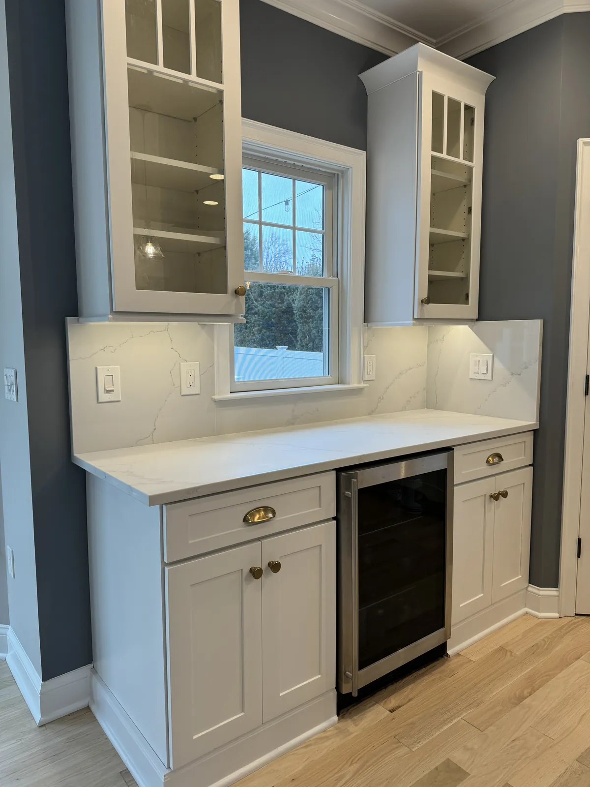 Wet bar backsplash in large-format marble-look tile around a window, above a white counter