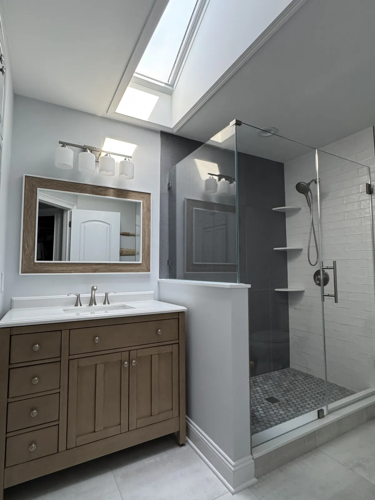 Walk-in shower with white subway tile, a charcoal accent wall, corner shelves and a hex mosaic floor, under a skylight