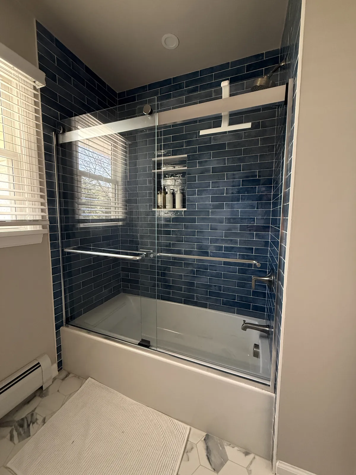 Tub surround tiled floor to ceiling in glossy blue glazed tile, with a recessed niche and a marble-look tile floor