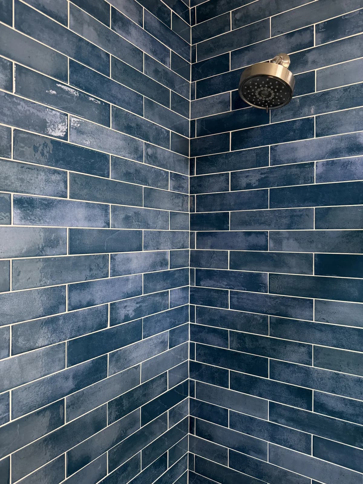 Corner of a shower in long blue glazed tile laid in a running bond, with tight, straight grout lines