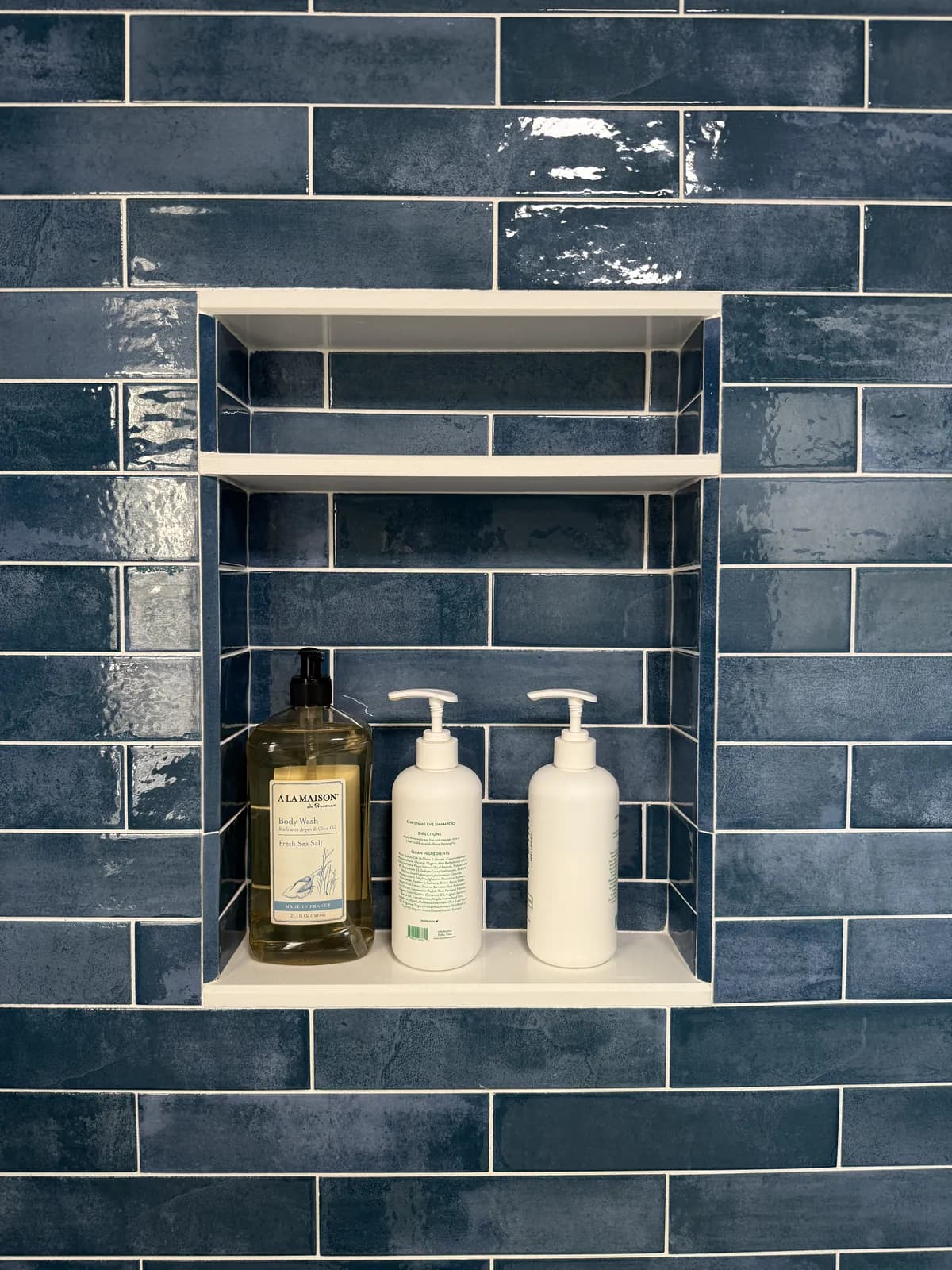 Recessed shower niche with a white shelf, framed in blue glazed tile with the grout lines carried straight through