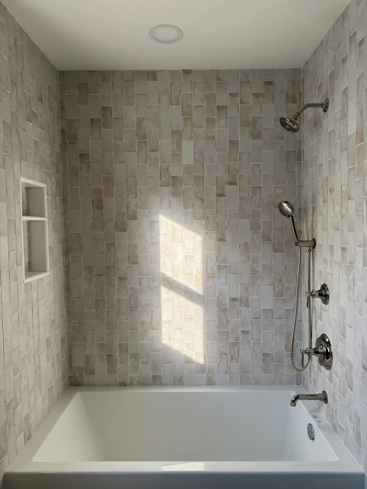 Tub surround in cream stone-look tile laid vertically, with a two-shelf recessed niche and brushed nickel fixtures