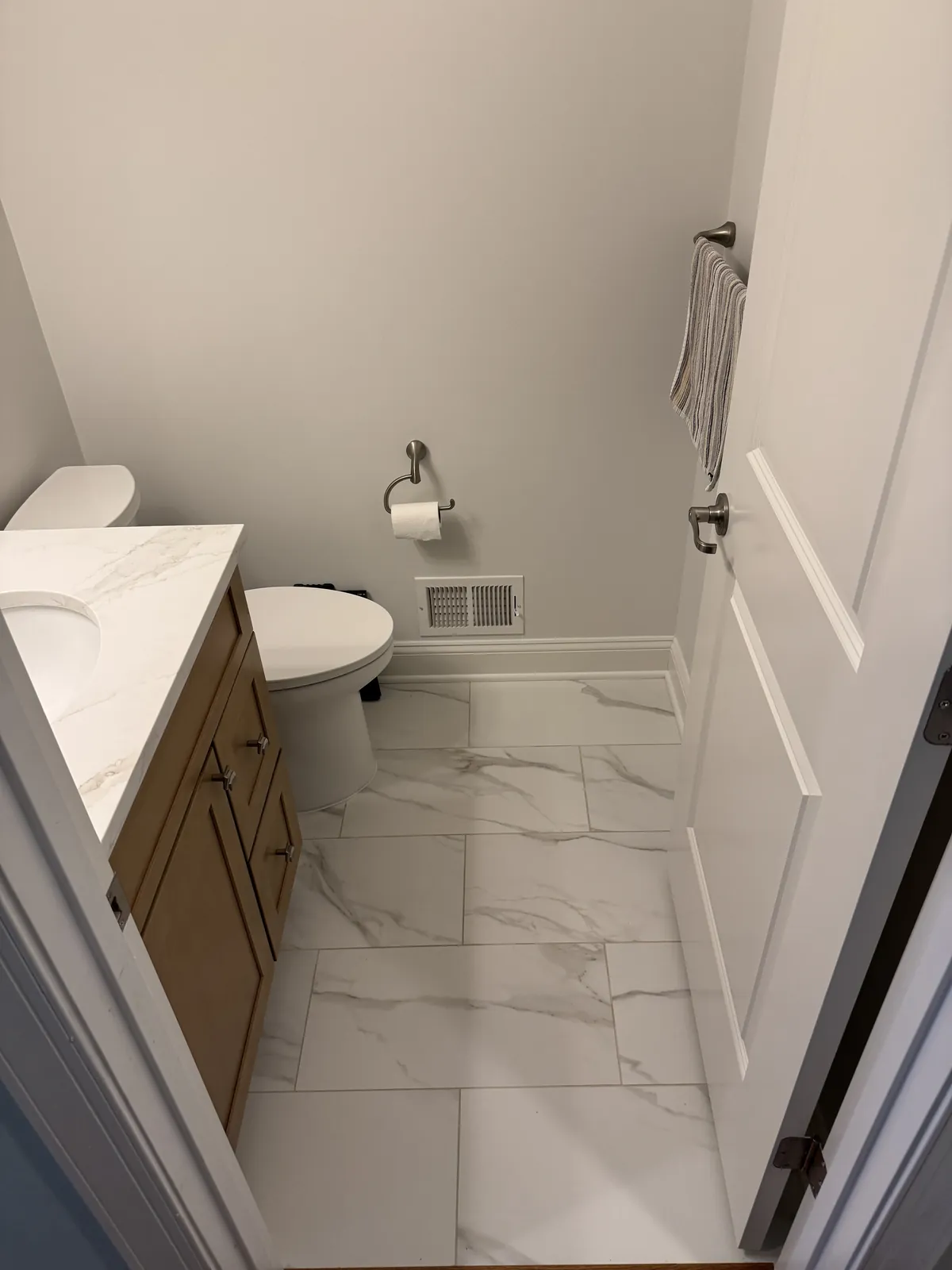 Half bath with large marble-look porcelain floor tile running from the door to the toilet