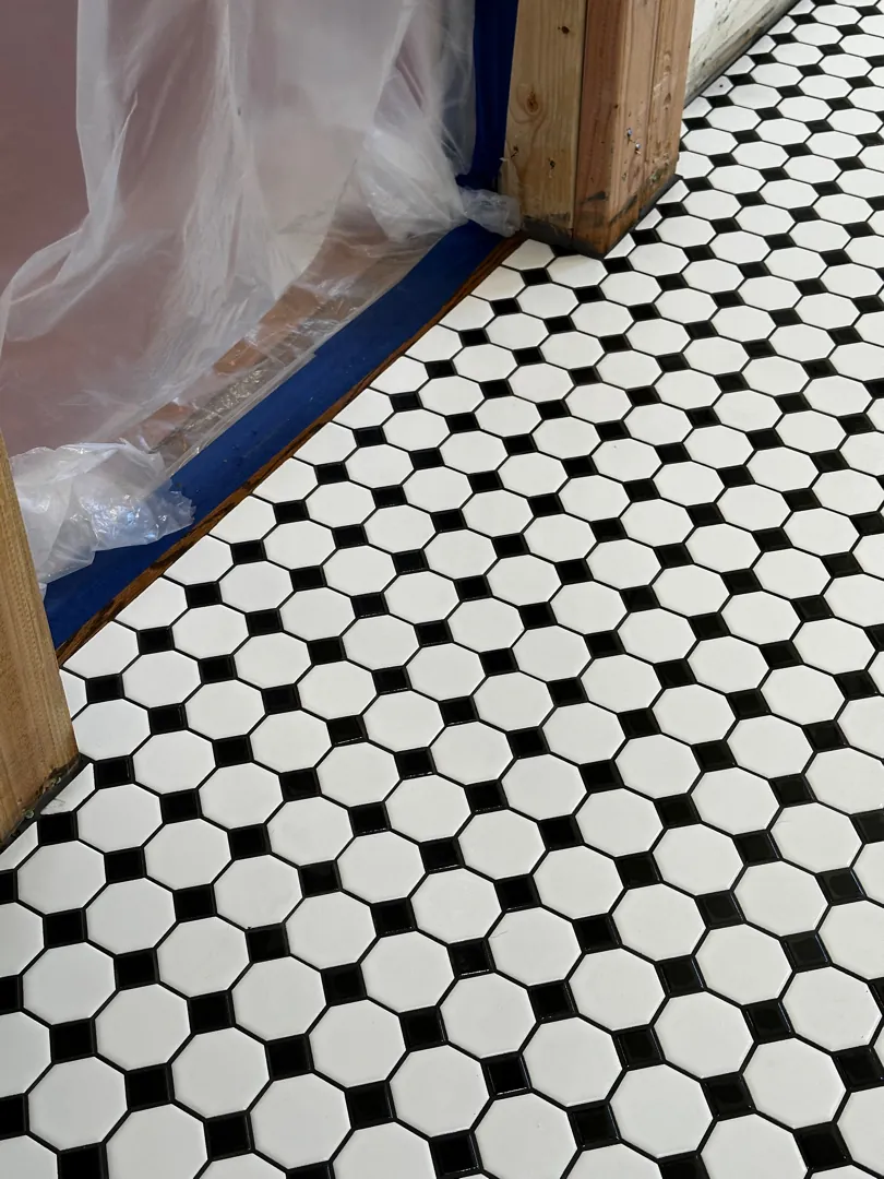Black and white octagon-and-dot mosaic floor tile, freshly set, with the doorway still protected in plastic