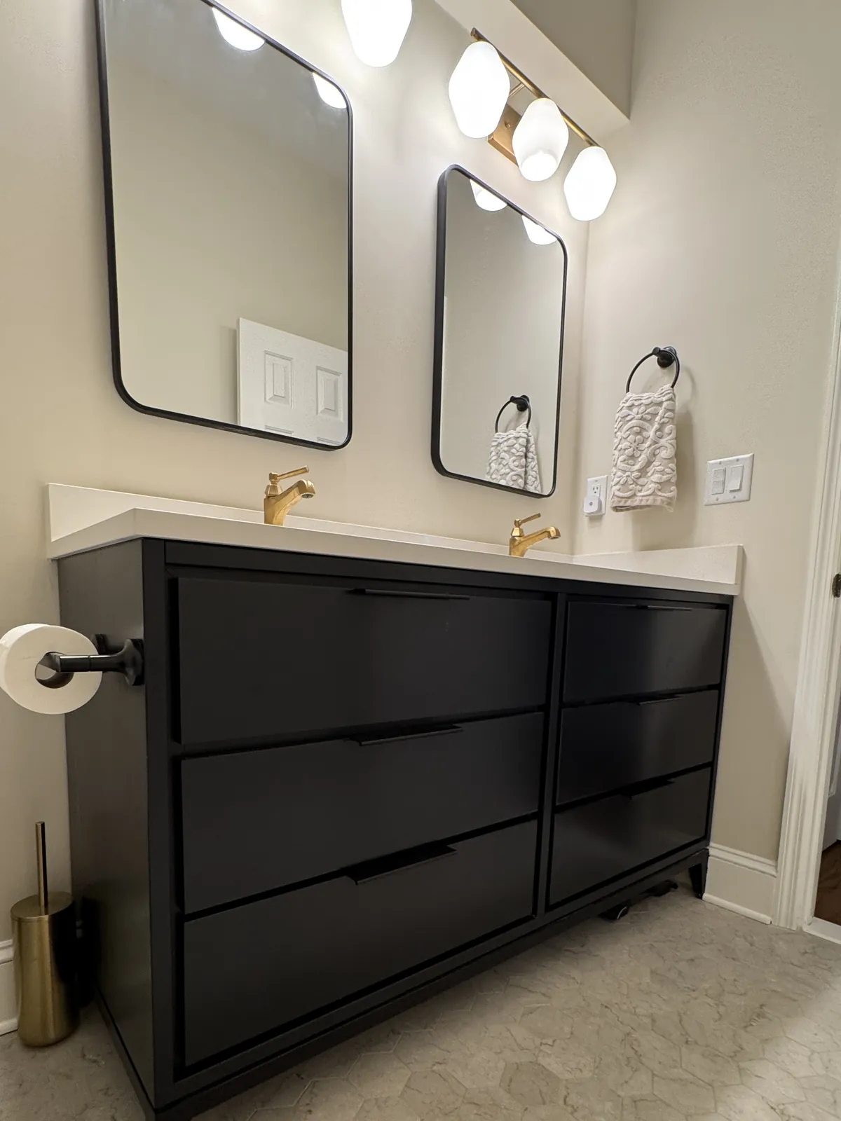 Black double vanity with brass faucets and matte black mirrors over a marble-look hexagon tile floor