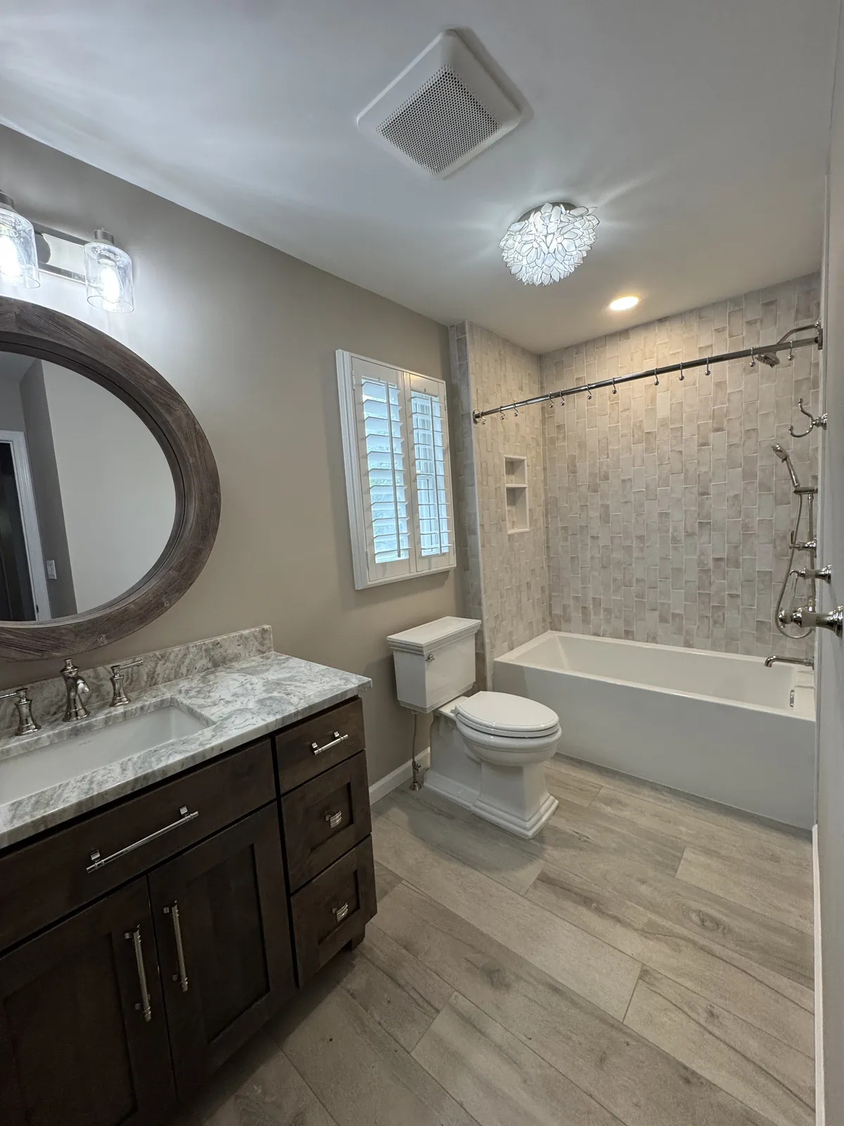 Bathroom with a dark wood vanity and oval mirror, a stone-look tiled tub surround and a wood-look tile floor