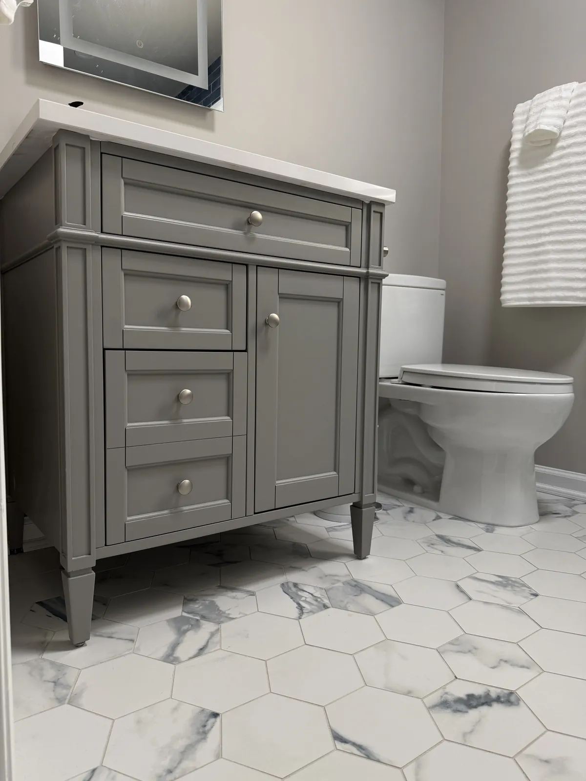 Large white and gray marble-look hexagon floor tile around a gray furniture-style vanity