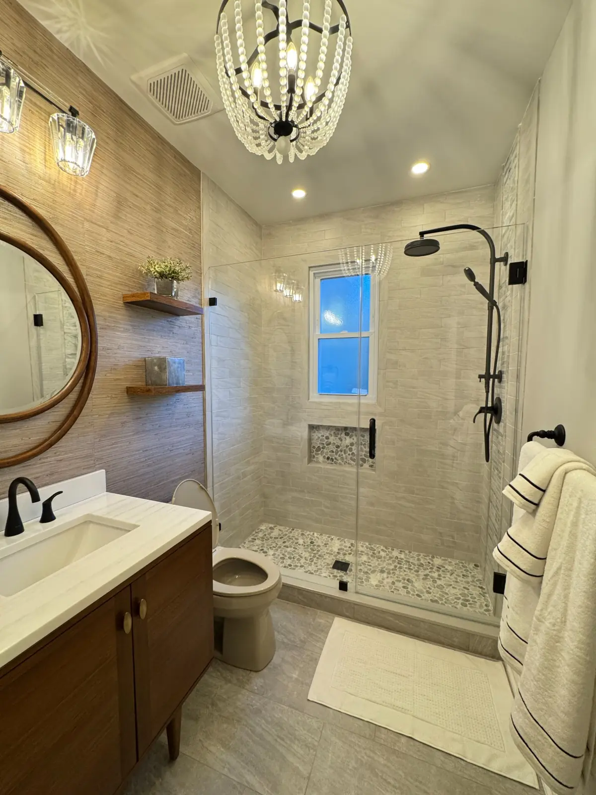 Bathroom with a round mirror, chandelier and a walk-in shower with two shower heads