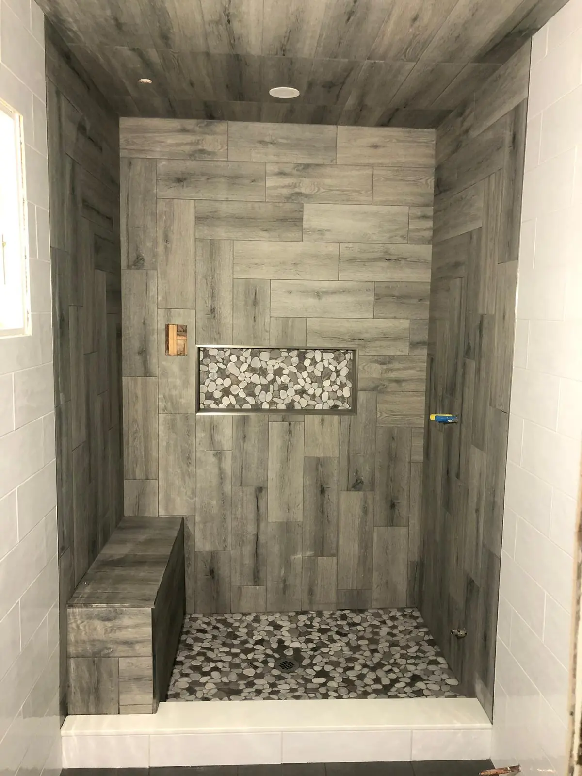 Walk-in shower tiled in wood-look plank with a pebble floor and a built-in bench