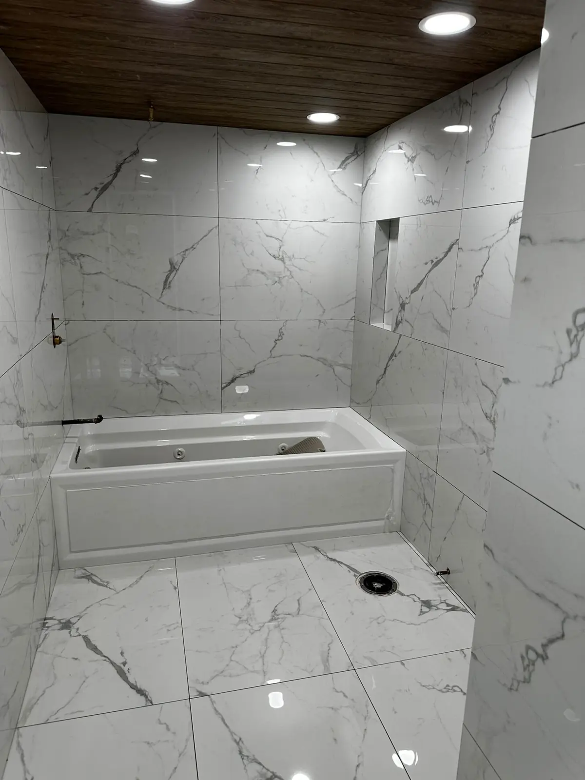 Marble tub surround and tiled walls beneath a wood-plank ceiling