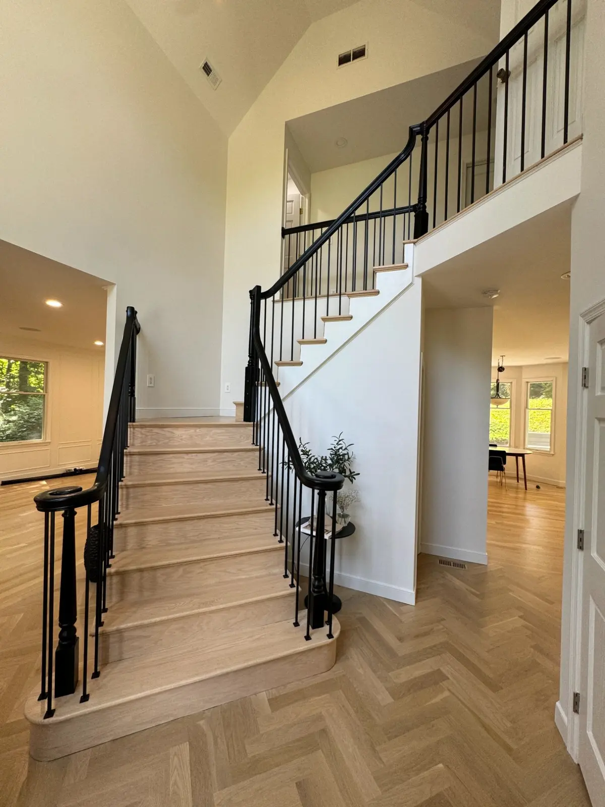 Two-storey entry with a herringbone wood floor, staircase and black iron railing