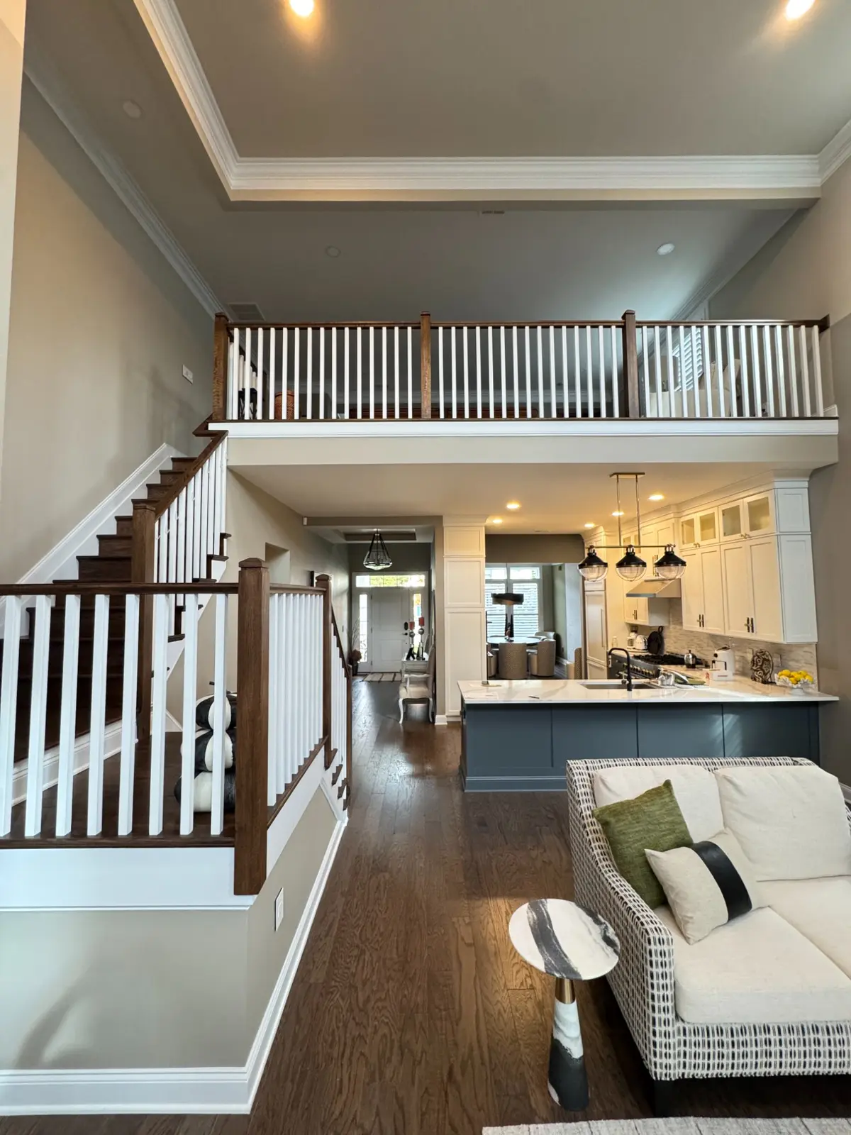 Two-storey foyer with a dark floor, white balusters and a kitchen visible beyond