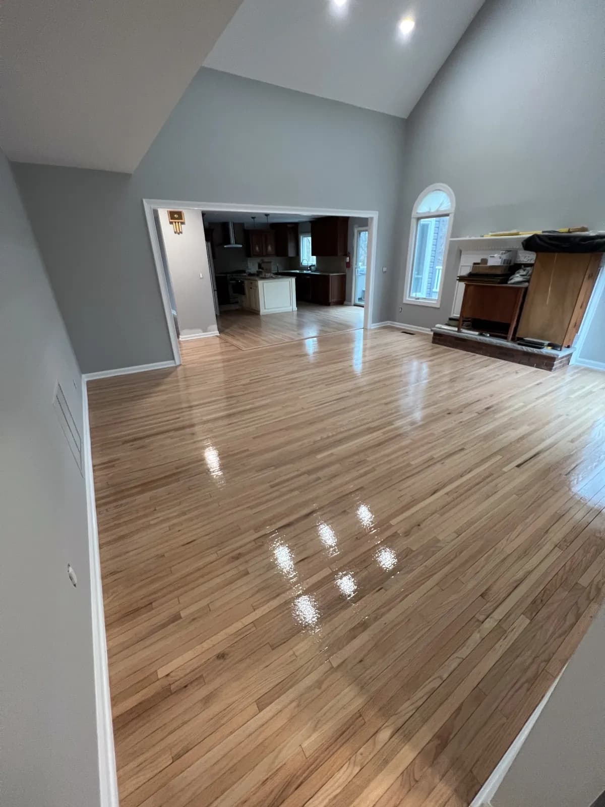 Open-plan room with a light oak floor, vaulted ceiling and a kitchen beyond