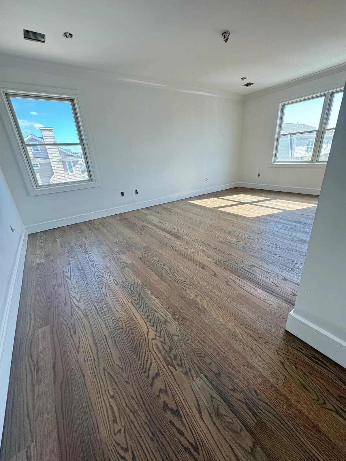 Refinished oak floor with afternoon sun falling across it from two windows