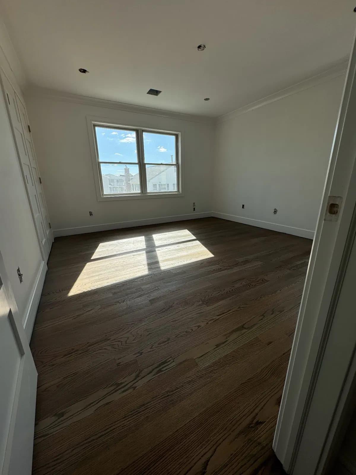 Dark walnut-toned floor with a bright patch of sunlight near the doorway