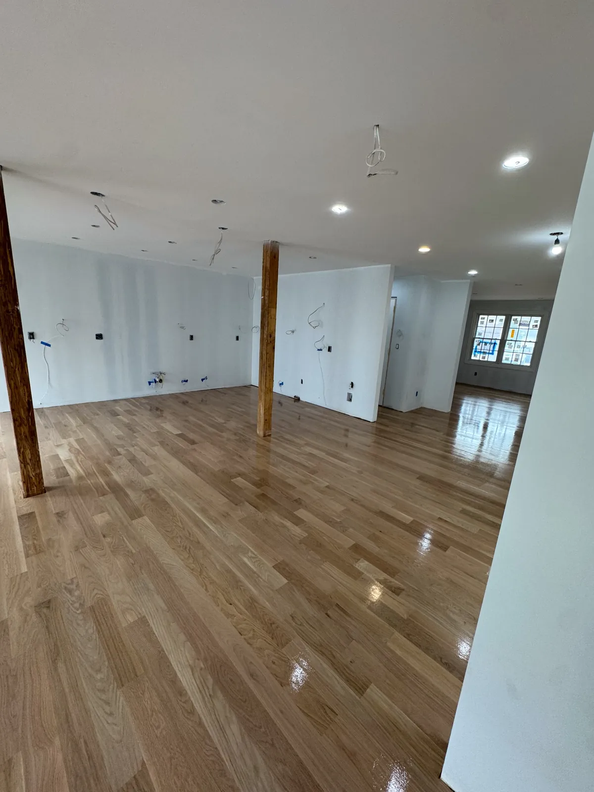 Newly finished light oak floor beside an exposed post and unpainted walls