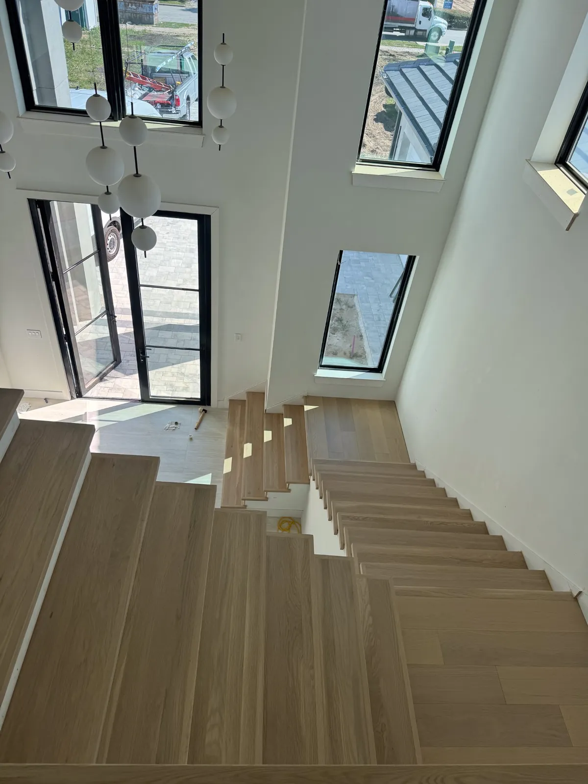 Modern staircase with pale oak treads beside a wall of black-framed windows