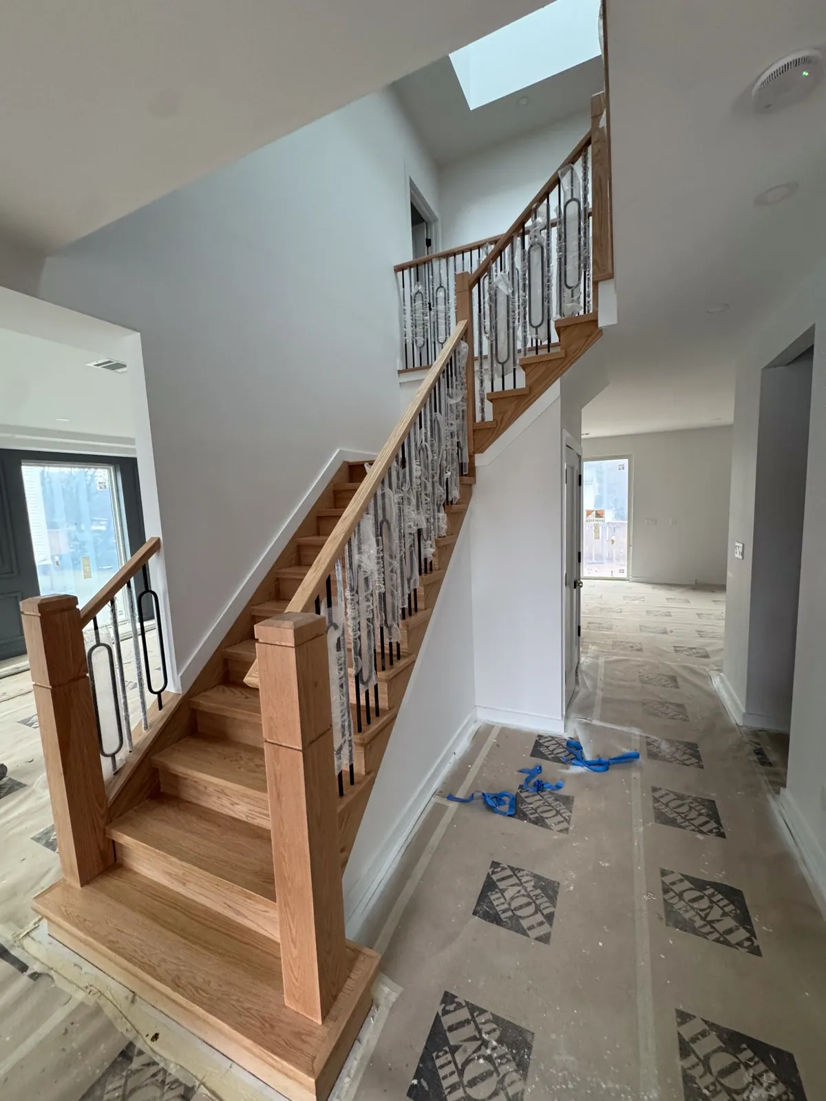 Oak staircase mid-installation, with the patterned tile floor of the hall below