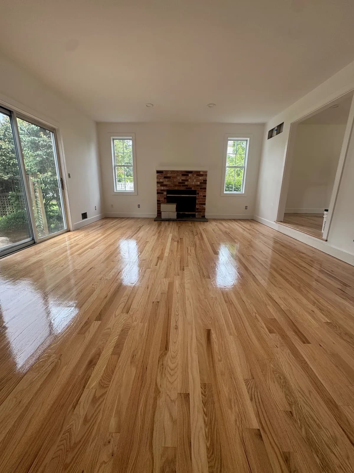 Large living room with a honey-toned oak floor, a brick fireplace and sliding doors to the garden