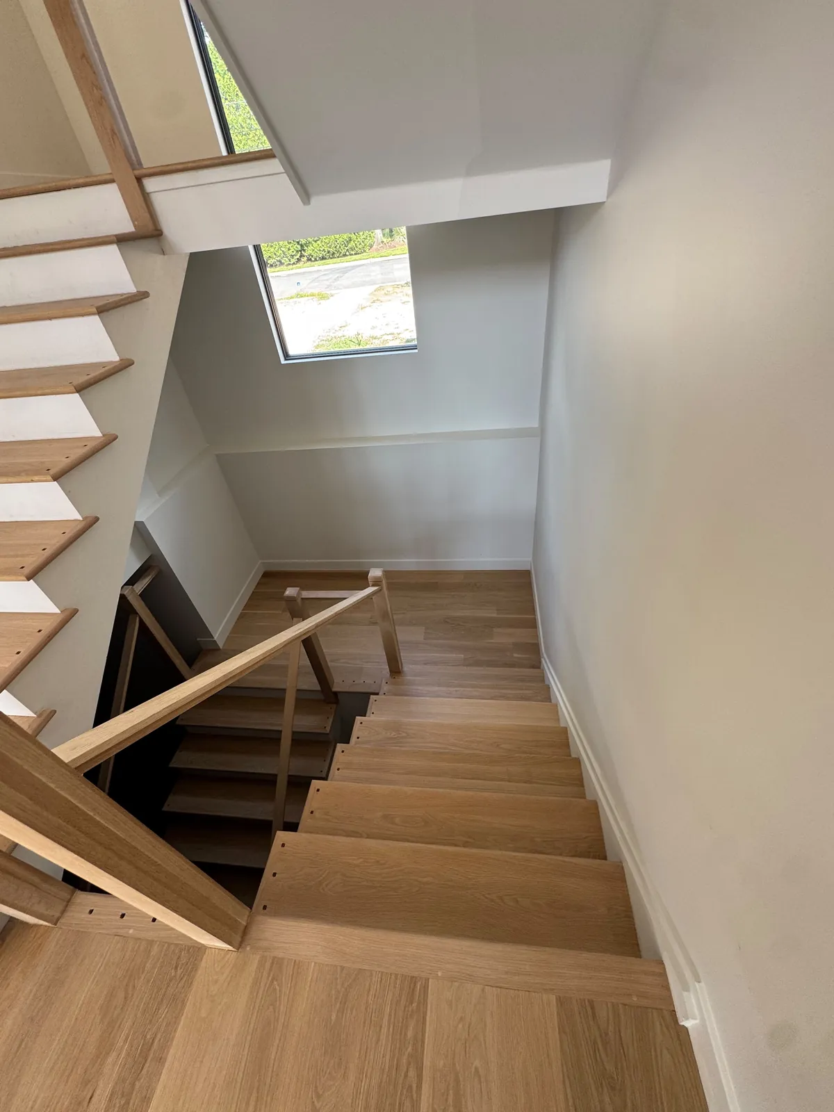Open-riser staircase with pale oak treads rising past a skylight