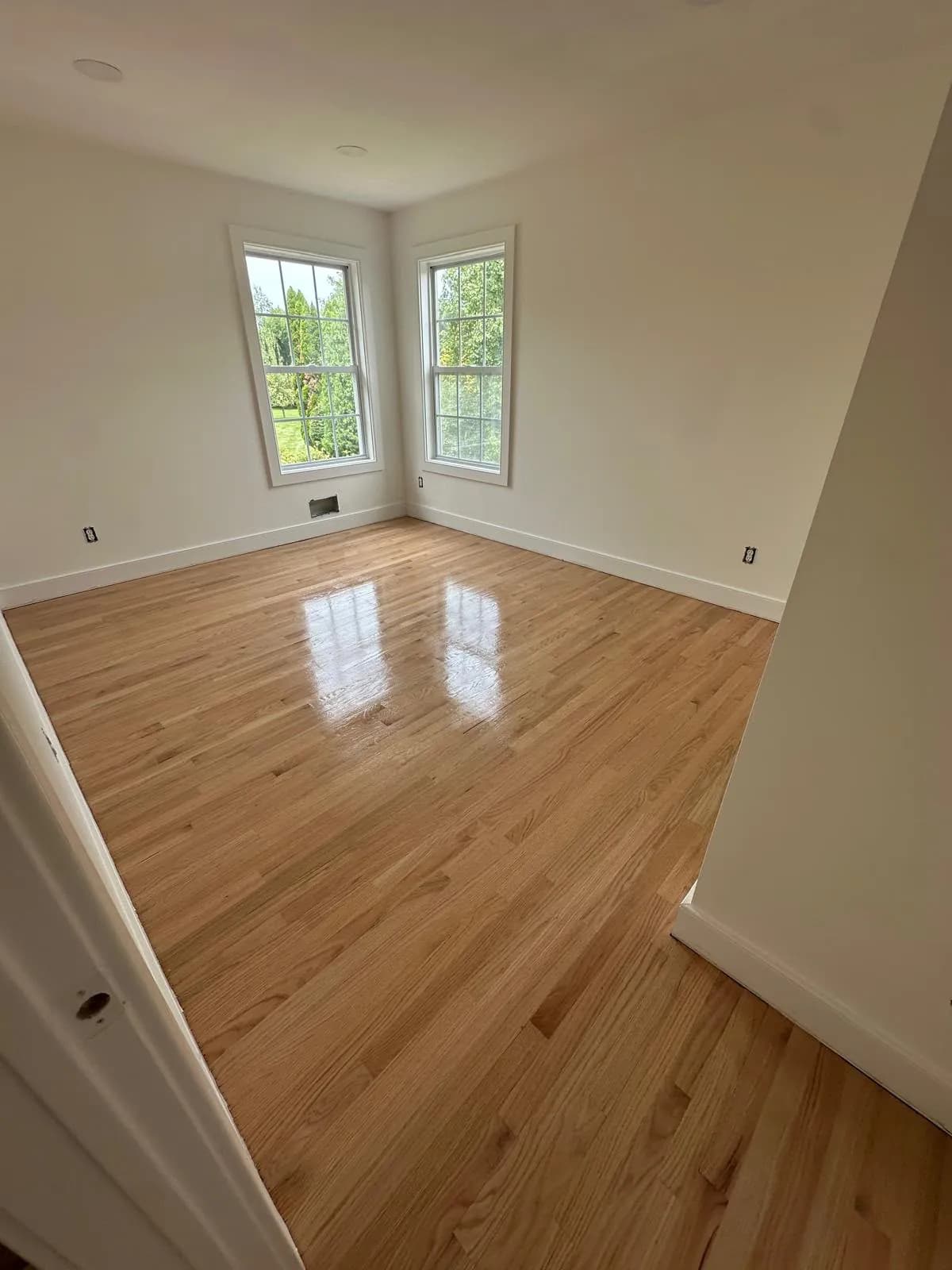 Honey-toned oak floor in a living room lit by two tall windows