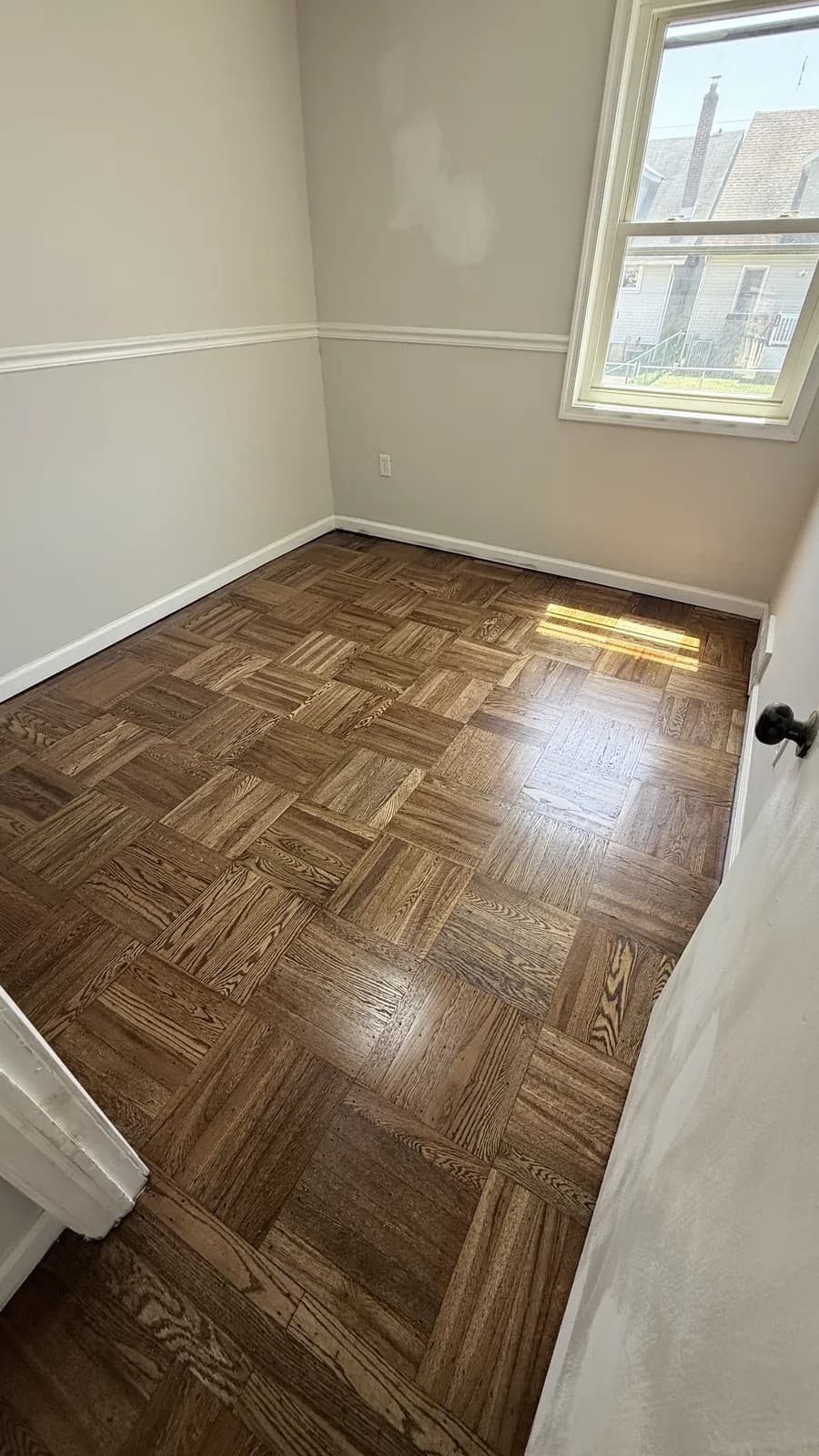 Corner of a room with dark basket-weave parquet and a chair rail