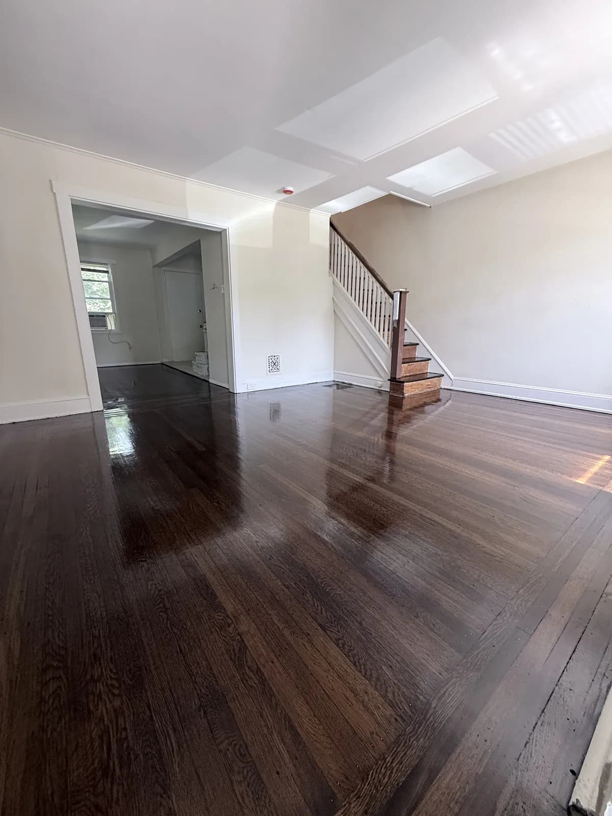 Dark-stained oak floor with a staircase and an open doorway to the kitchen