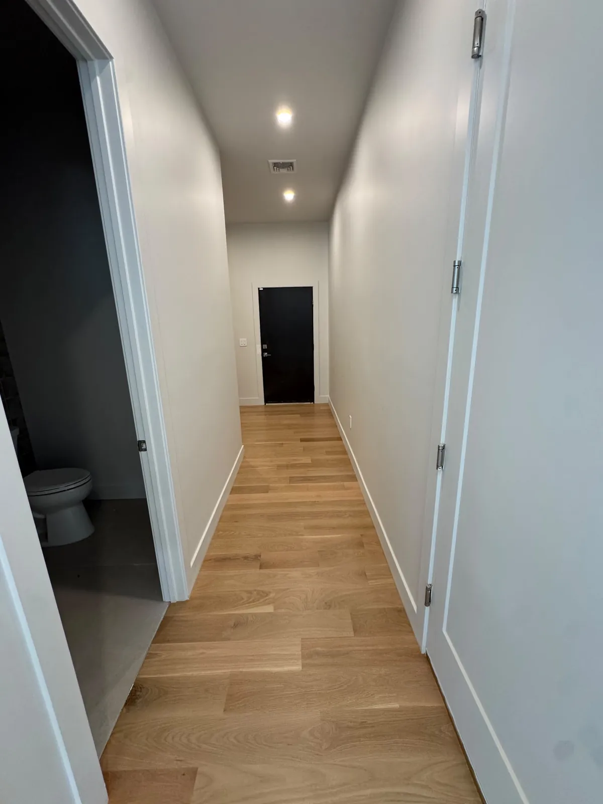 Pale oak hallway with a bathroom door open on one side and a dark door at the end