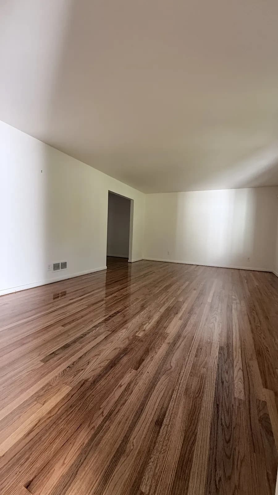 Medium-toned oak floor in an empty living room with a doorway beyond