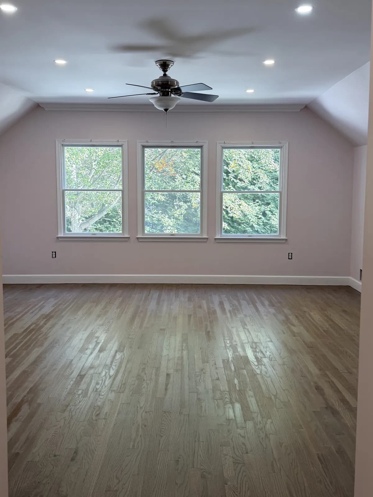 Oak floor refinished in a gray-brown stain in a long upstairs room with three windows
