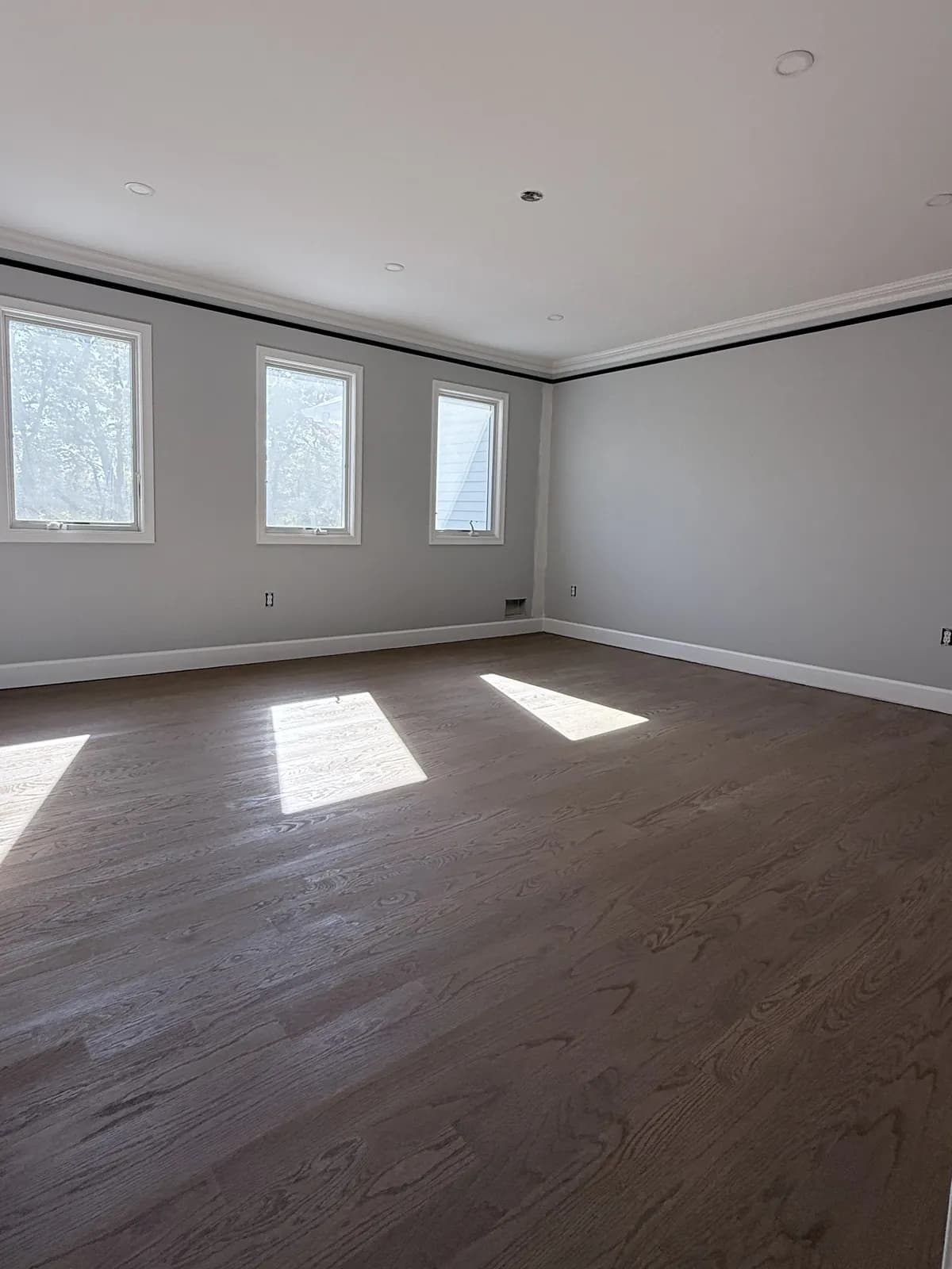 Dark-stained oak floor with squares of sunlight from three windows