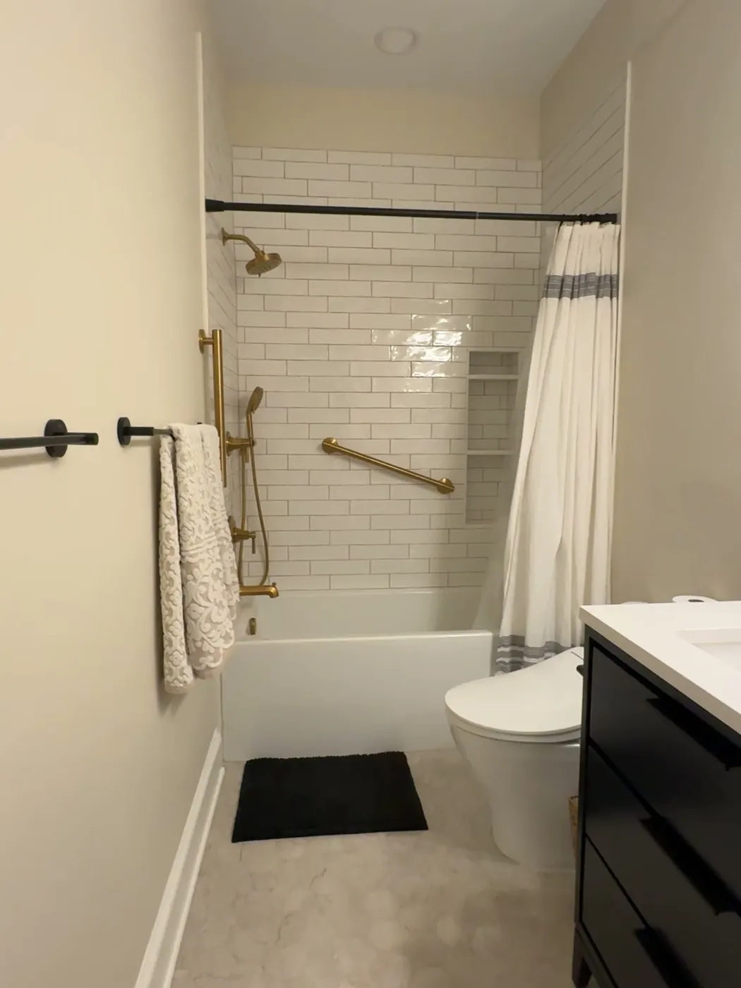 After: the same bathroom from the doorway with a subway tile tub, hexagon floor tile and a black double vanity, by Summit Home Services