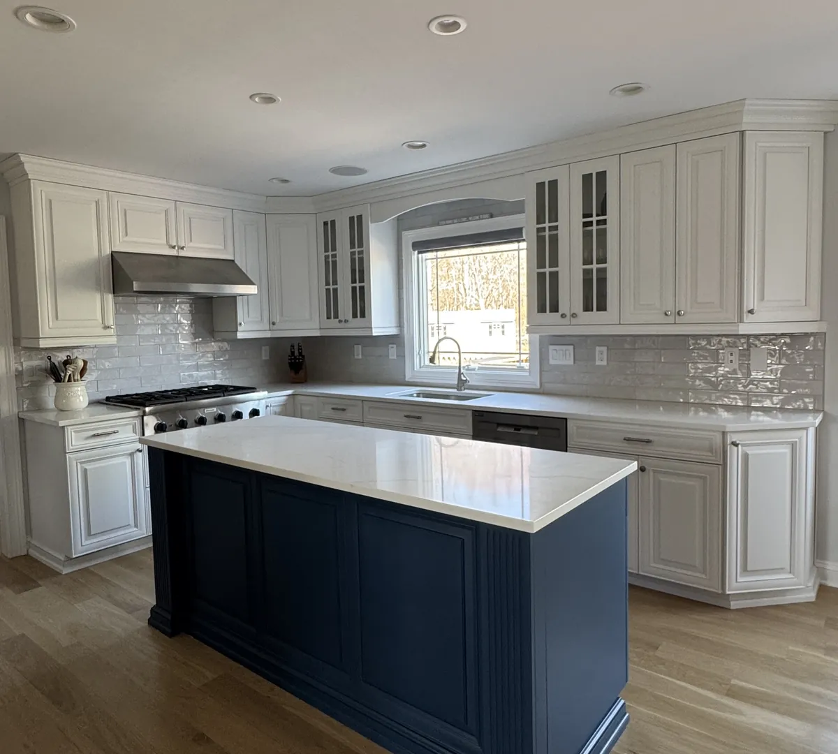 After: the same kitchen with white cabinets, a navy island and a glazed white subway tile backsplash, by Summit Home Services
