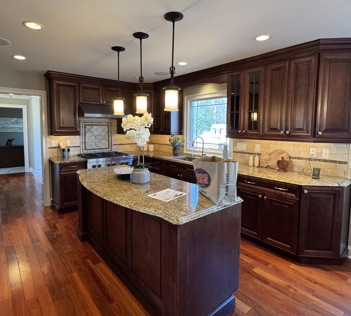 Before: a cherry kitchen with a tumbled stone backsplash, a granite island and three pendant lights