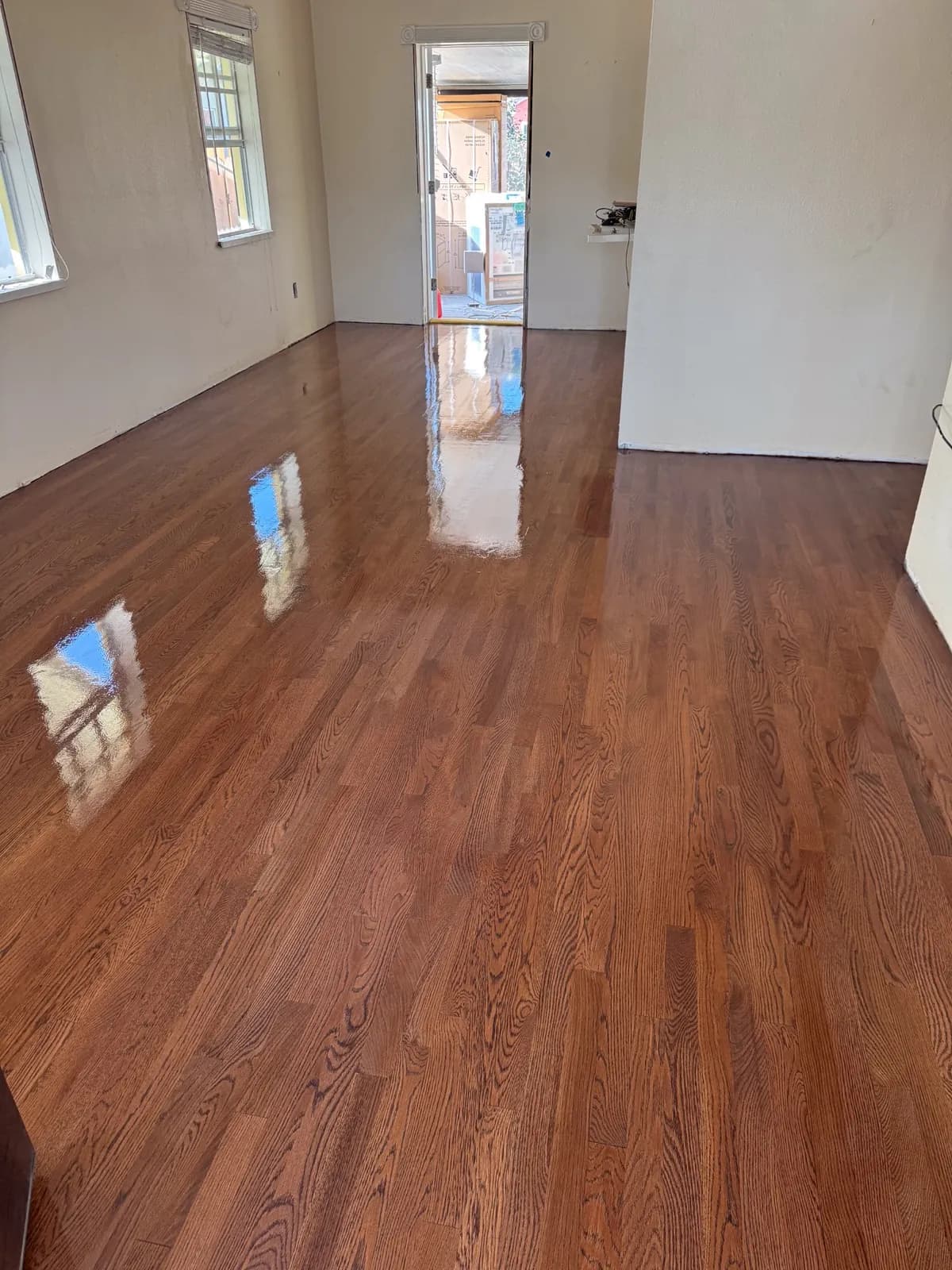 Refinished red oak floors with a high-gloss finish reflecting the windows