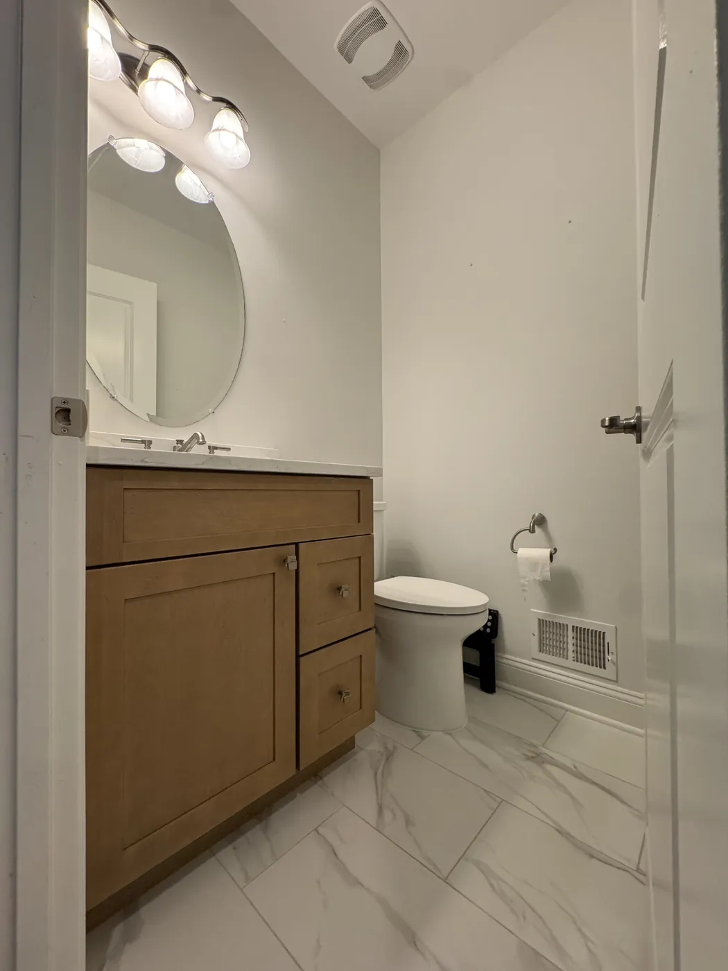 After: the same half bath with a marble-look porcelain floor, a wood vanity and fresh white walls, by Summit Home Services