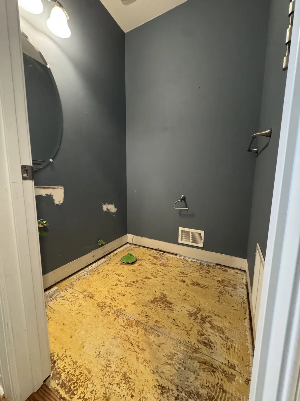 Before: a half bath seen from the doorway with the floor down to bare subfloor and the vanity and toilet removed