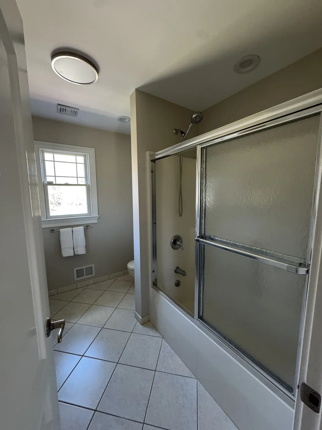 Before, seen from the doorway: a one-piece fiberglass tub surround behind a glass slider door and white floor tile in a Middletown NJ bathroom