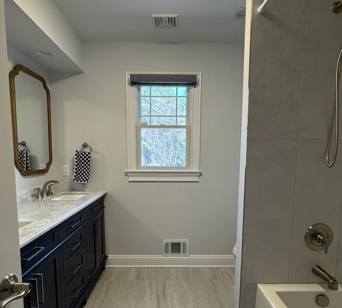 After: the same bathroom with a tiled tub, a navy double vanity and a gray plank-look tile floor running to the window, by Summit Home Services