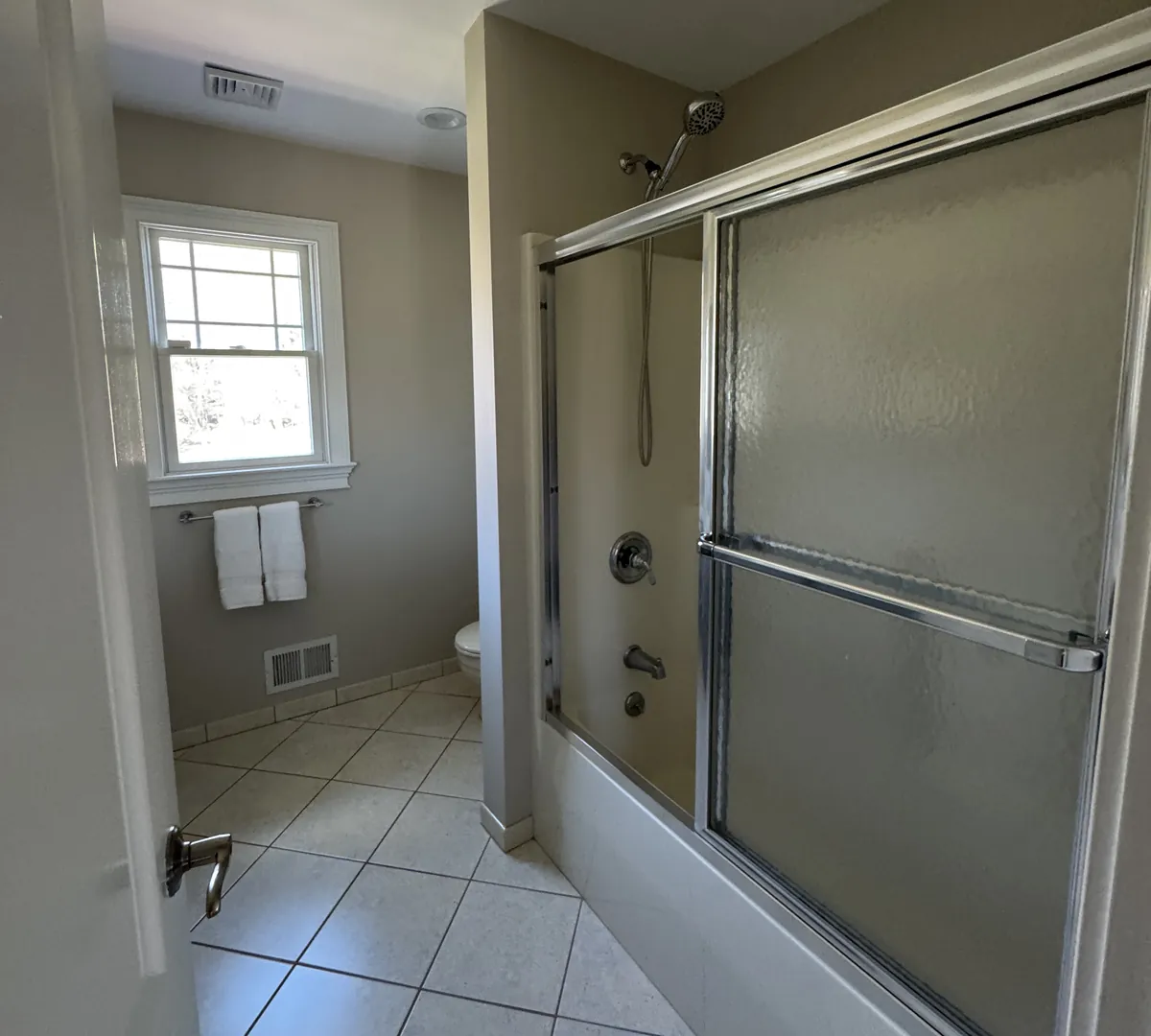 Before: a bathroom seen from the door with a sliding-glass tub enclosure on the right and white diagonal floor tile