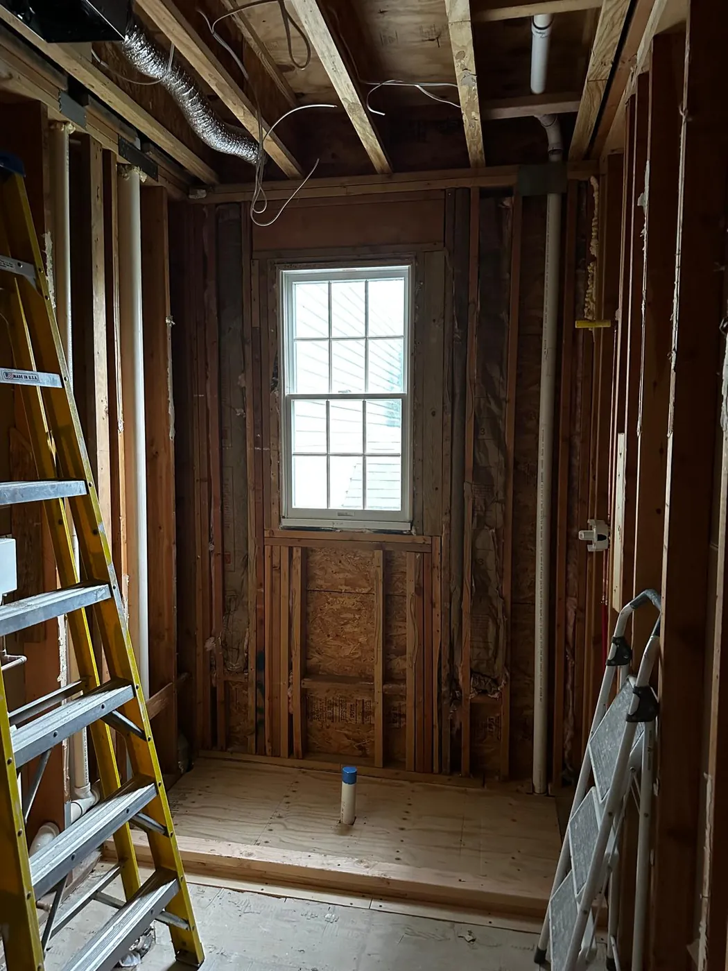 Before: shower area stripped to the wall framing and subfloor, with the window in the back wall